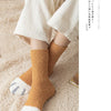 A pair of tan plush socks with white cat paw prints are shown on a person's feet against a light beige background.