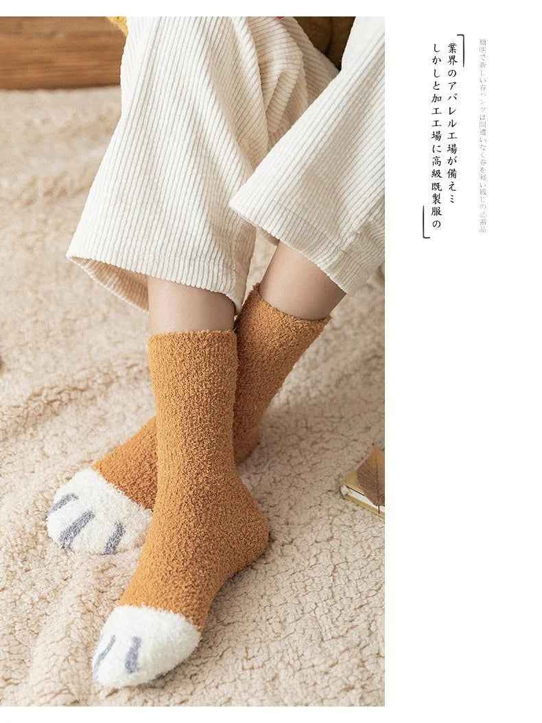 A pair of tan plush socks with white cat paw prints are shown on a person's feet against a light beige background.