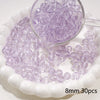A clear glass measuring spoon holds purple spacer beads scattered on a white dish.