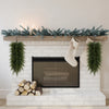 A long green artificial Christmas teardrop swag with Norfolk pine needles displayed on a white brick fireplace mantel.