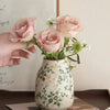 A hand holds a vase of pink roses in a handmade ice crackle ceramic vase with green foliage.
