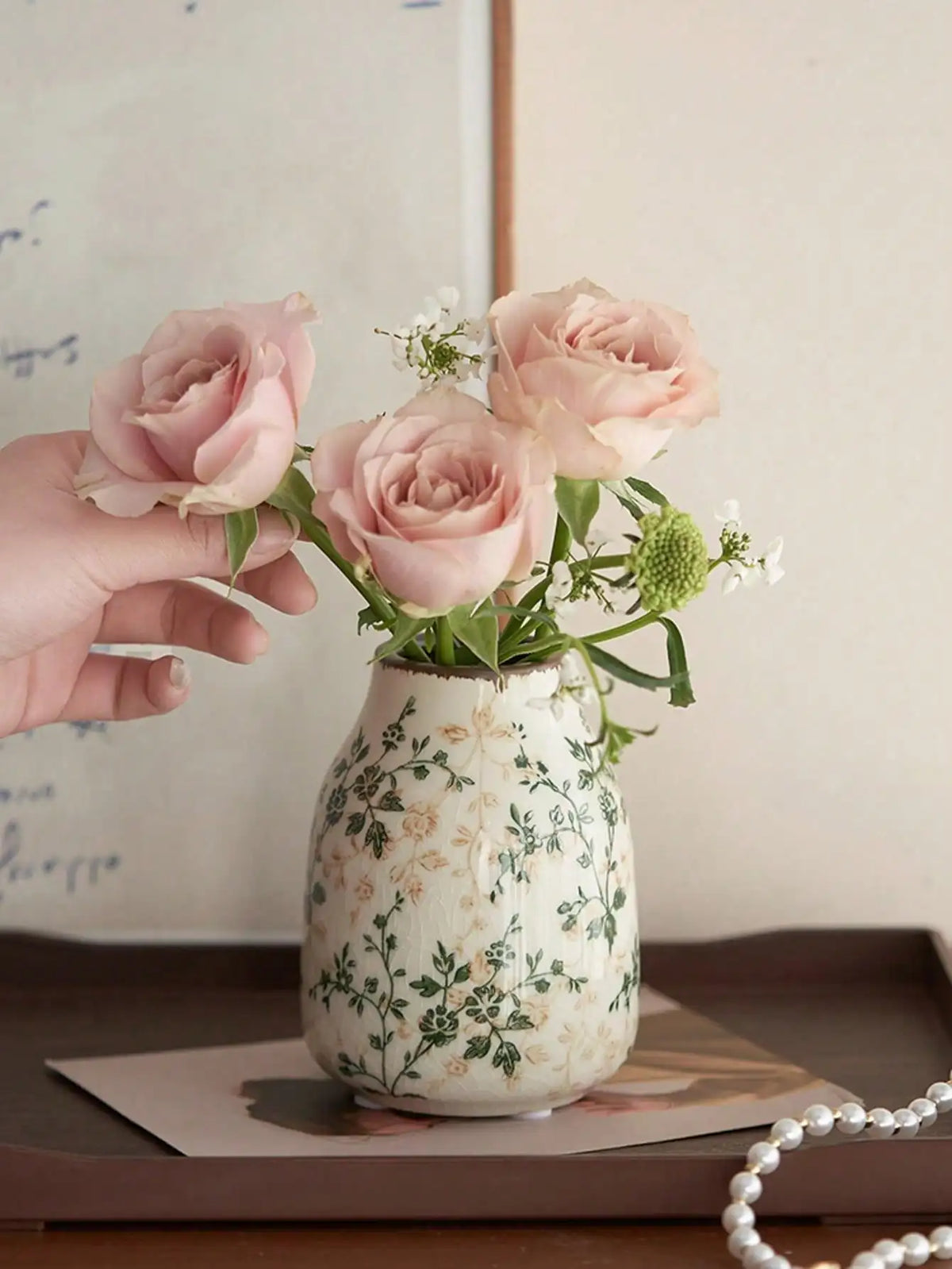 A hand holds a vase of pink roses in a handmade ice crackle ceramic vase with green foliage.