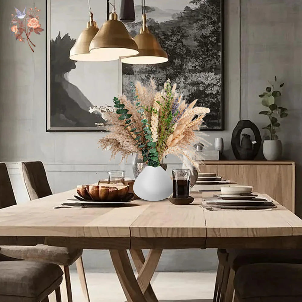 A centerpiece featuring a bouquet of natural dried eucalyptus flowers on a wooden dining table.