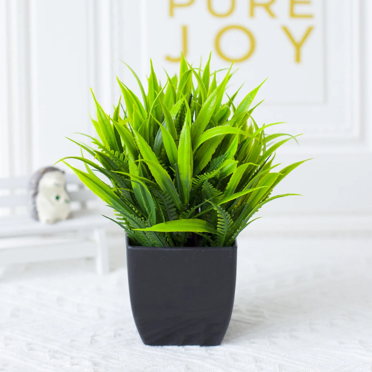 A vibrant green artificial eucalyptus plant in a black pot displayed on a white surface.