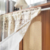 Beige sheer curtain with floral embroidery hanging on a wooden rack.