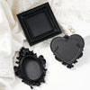 Black resin wall decor pendants in various ornate frames and heart shapes displayed on white fabric