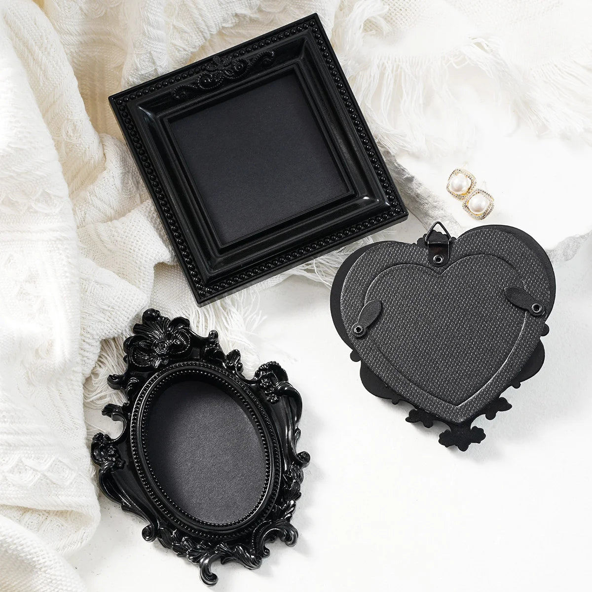 Black resin wall decor pendants in various ornate frames and heart shapes displayed on white fabric