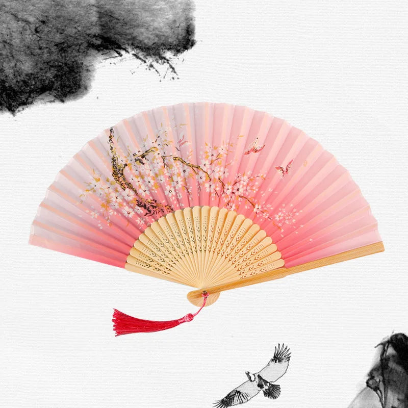 A vintage bamboo folding hand fan with pink and gold accents, featuring delicate floral designs.