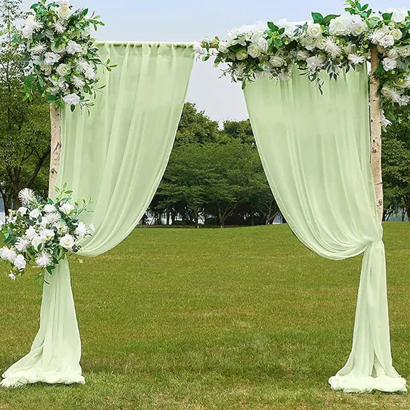 A light green chiffon backdrop curtain decorated with white flowers framing an outdoor event setting.