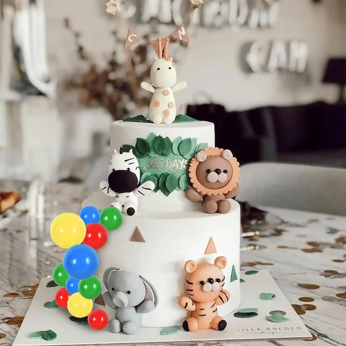 A white tiered cake decorated with natural green leaves and animal-themed foam ball toppers.