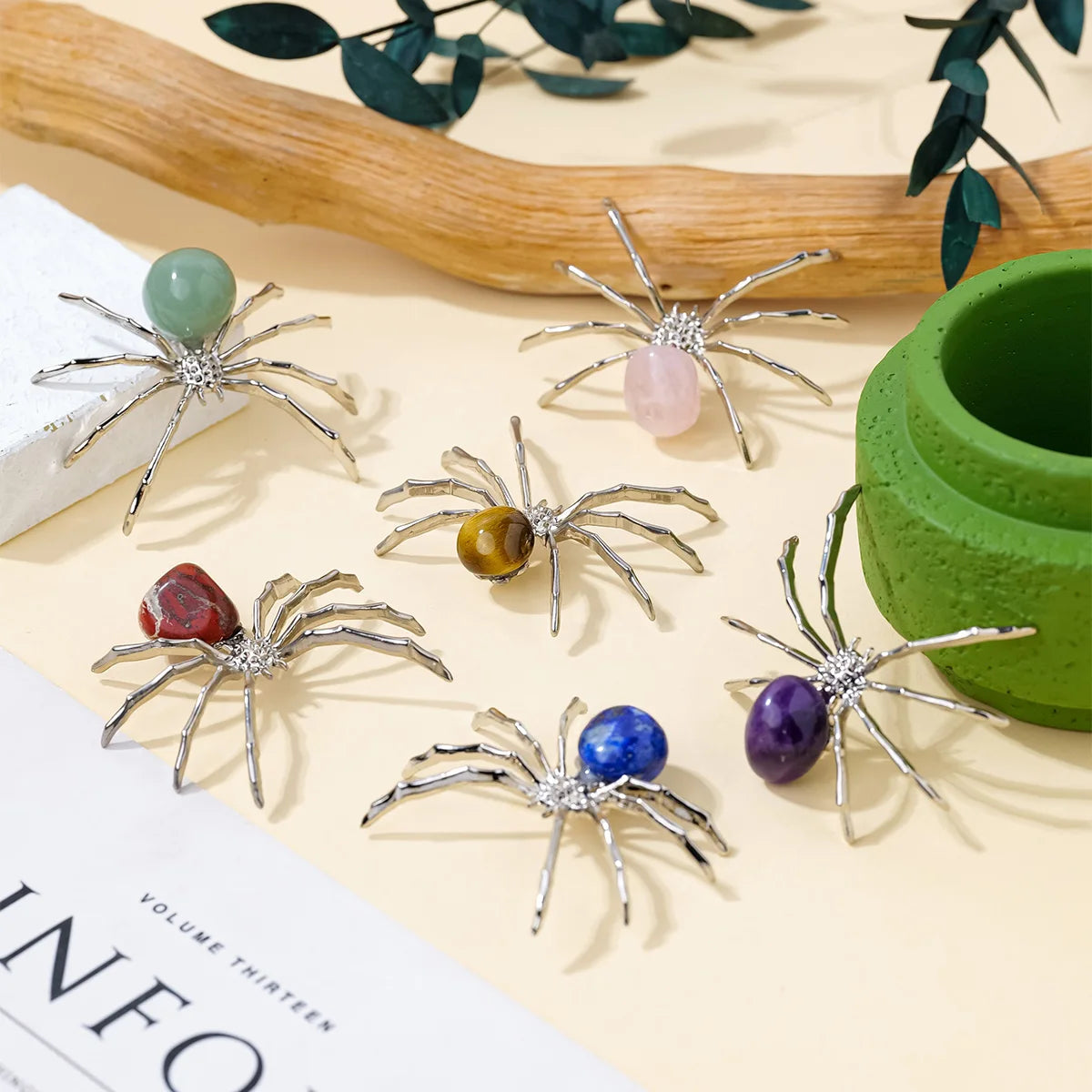 Handcrafted crystal spider figurines in various colors like green, pink, amber, and purple displayed on a light background.