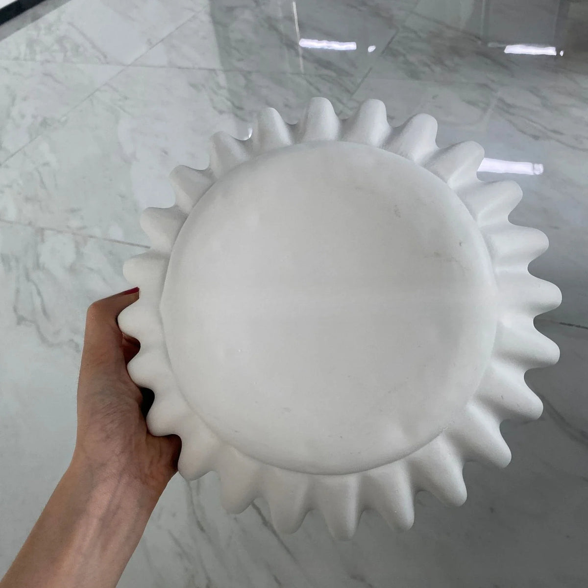 A white lotus leaf resin decorative bowl with a sunburst pattern is held against a marble background.