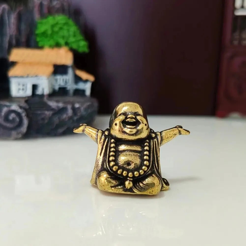 A small brass statue of a laughing Buddha with arms outstretched sitting on a white surface.