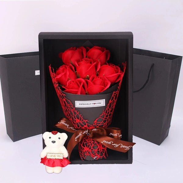 A black gift box contains a bouquet of red roses and a small teddy bear gift.