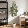 A tall artificial olive tree with green leaves stands in a white pot next to a modern wooden desk.