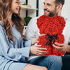 Eine Frau und ein Mann lächeln, während sie einen künstlichen roten Rosen-Teddybären halten.