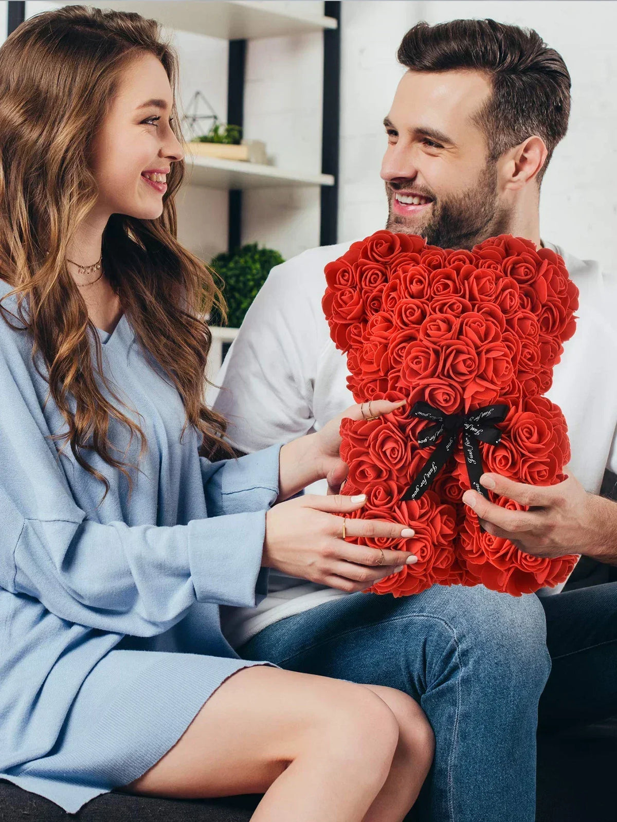 Eine Frau und ein Mann lächeln, während sie einen künstlichen roten Rosen-Teddybären halten.