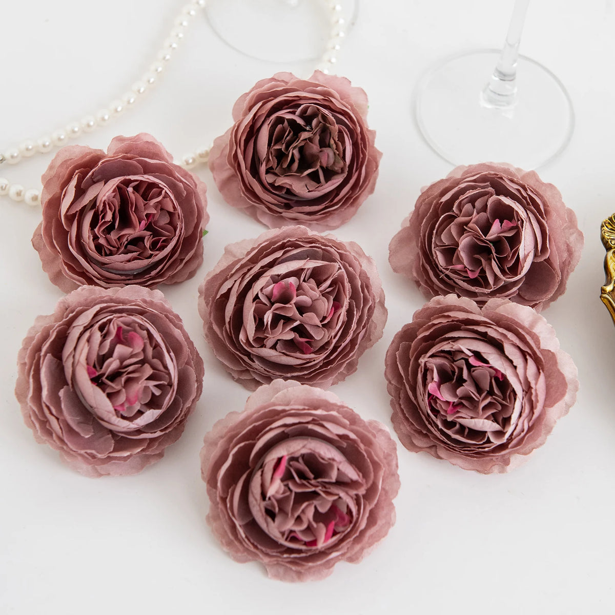 A cluster of dried silk peony artificial flowers in dusty rose and mauve tones arranged on a white surface.