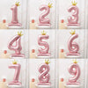 A set of large pink foil number balloons from 1 to 9 displayed on white pedestals.