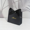 A black paperboard thank you gift bag tied with a black ribbon and gold script reading Merci.