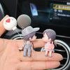 A small figurine of a couple with a balloon, featuring a male figure in a cap and a female figure, displayed on a hand.