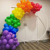 A large arc of vibrant latex balloons in shades of orange, yellow, green, and purple is displayed against a white door.