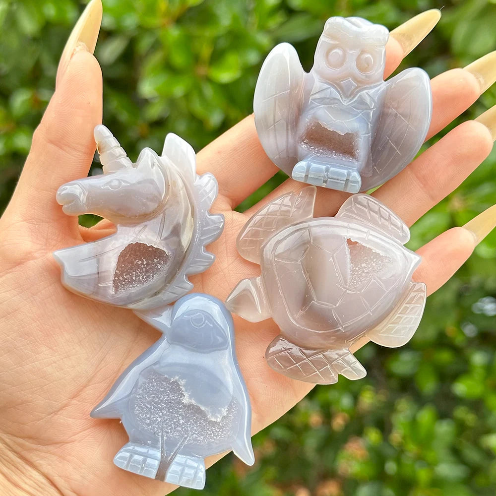 A set of natural agate crystal figurines shaped like a unicorn, an owl, and a penguin held in a hand.