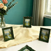 A collection of vintage baroque resin picture frames in green and gold set on a white table with roses and sheer curtains in 