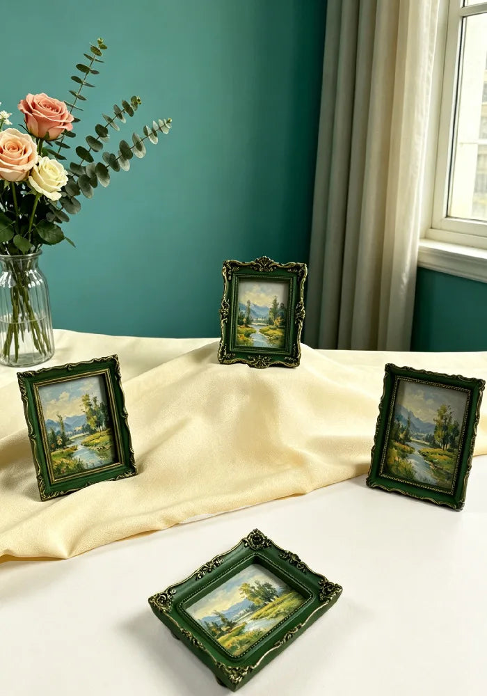 A collection of vintage baroque resin picture frames in green and gold set on a white table with roses and sheer curtains in 
