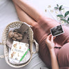 A hand holds an ultrasound photo inside a woven basket filled with baby memory items and a journal.