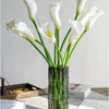 A bouquet of twelve white calla lily artificial flowers in a dark glass vase.
