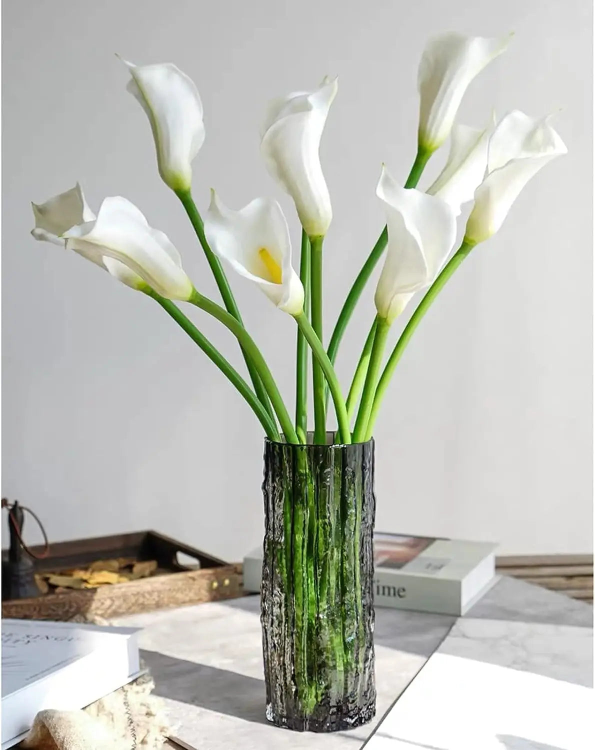 A bouquet of twelve white calla lily artificial flowers in a dark glass vase.