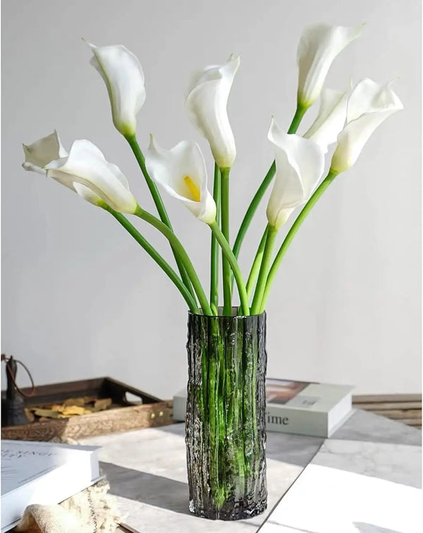 A bouquet of twelve white calla lily artificial flowers in a dark glass vase.