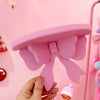 A hand holds a pink bow-shaped wooden shelf mounted on a pink wall.