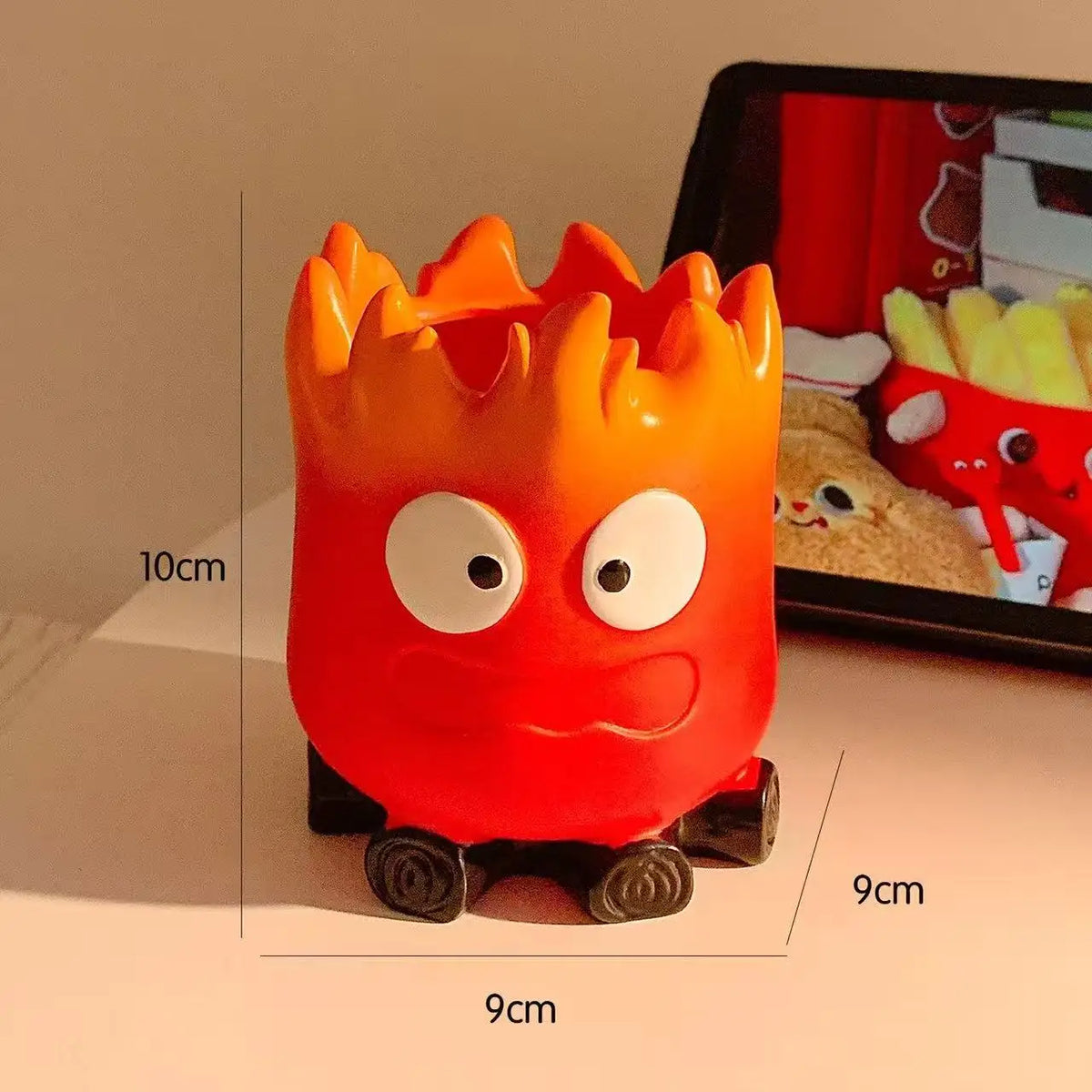 A bright orange resin fire spirit figurine used as a desk organizer or key tray.