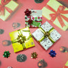 A collection of holographic star gift bows and wrapped gifts in red, green, and gold on a pink background.
