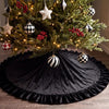 A dark velvet Christmas tree skirt decorated with silver and black geometric ornaments and a ruffled edge.