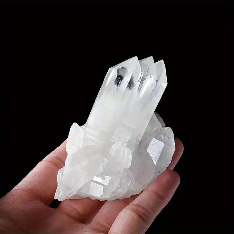 A hand holds a cluster of clear quartz crystals against a black background.