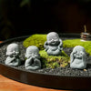 A collection of small, grey stone monk statues for meditation and Zen decor placed on mossy ground in a dark bowl.
