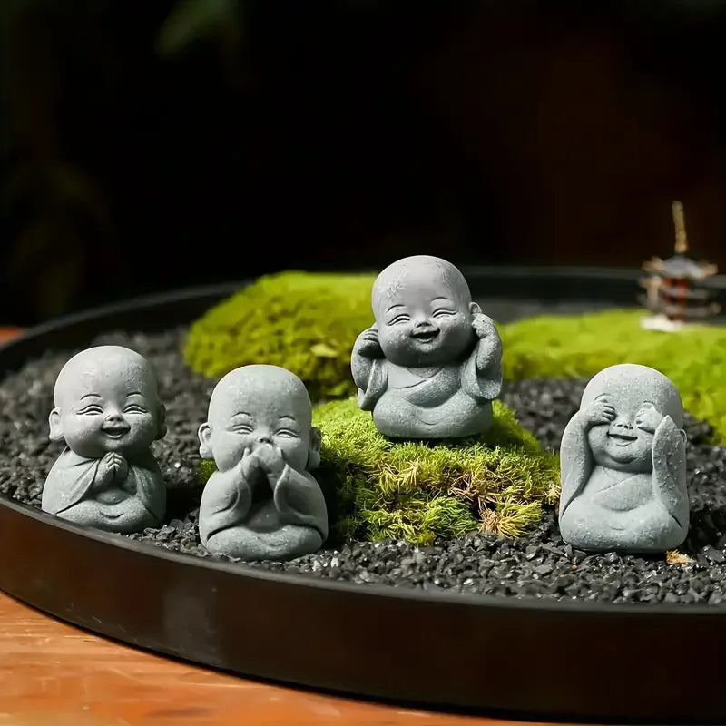 A collection of small, grey stone monk statues for meditation and Zen decor placed on mossy ground in a dark bowl.