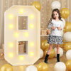 A young girl stands next to a large white LED light-up number decoration shaped like a house, surrounded by yellow and white 