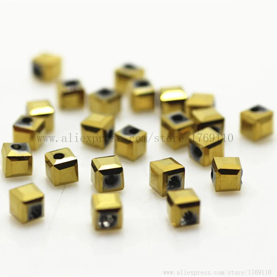 A collection of small, square-cut glass crystal beads in gold color scattered on a white surface.