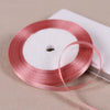 A roll of pink satin ribbon on a white spool resting on a light-colored surface.