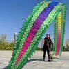 Una persona sostiene un gran y colorido aderezo para fitness de danza de dragón con escamas verdes y moradas contra un cielo 