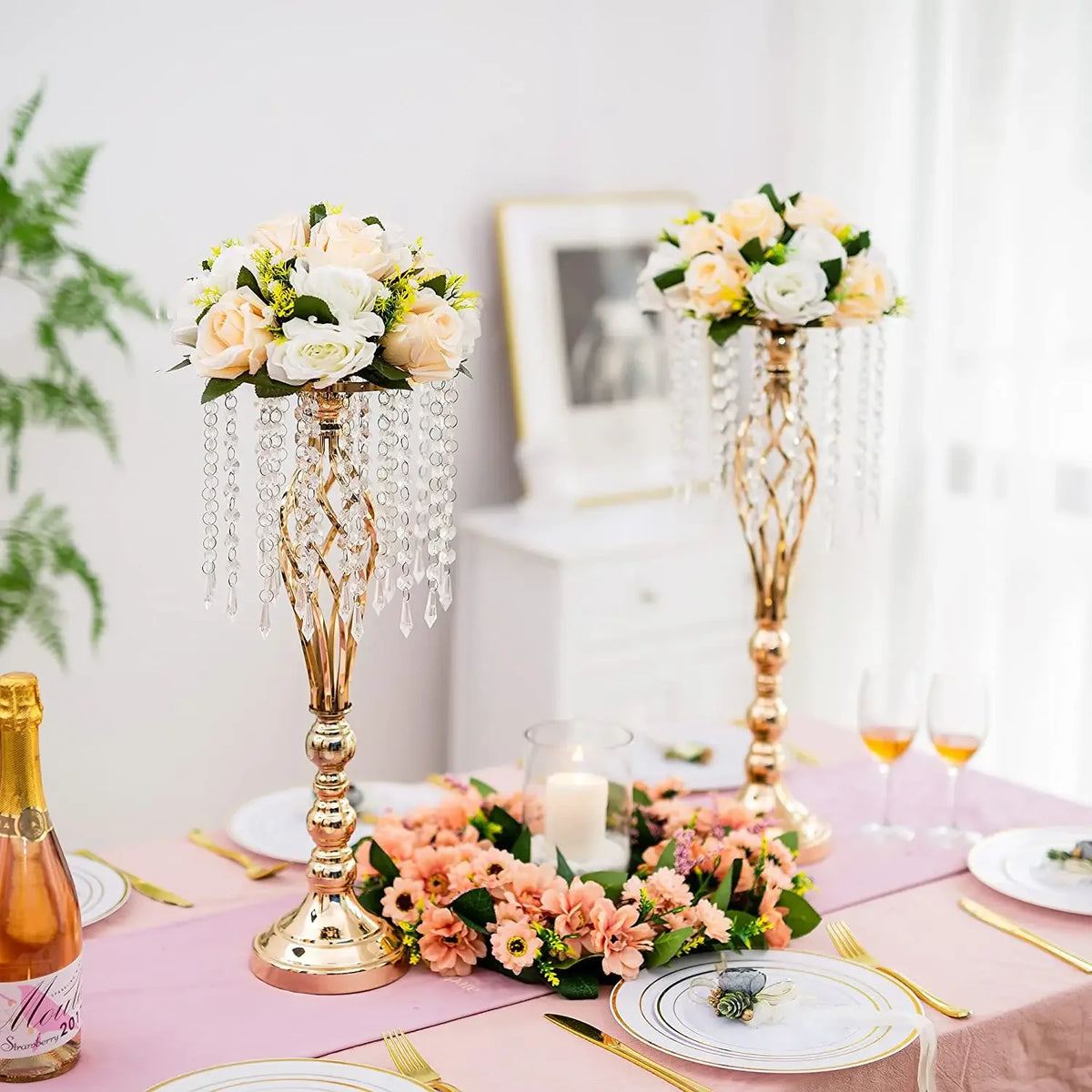 Gold crystal vase set with floral arrangements and cascading crystals on a pink table.