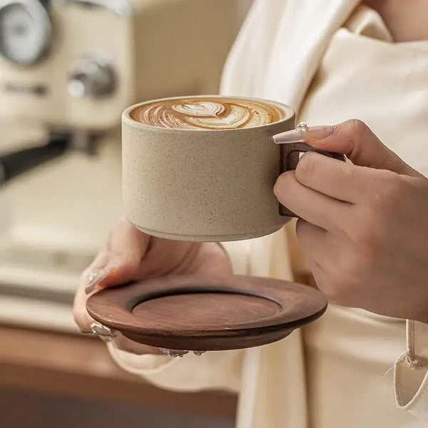 A hand holds a beige ceramic coffee cup with latte art and a matching saucer.