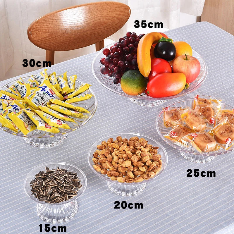 A collection of various foods including fruit, nuts, and yellow snacks displayed on clear acrylic serving plates.