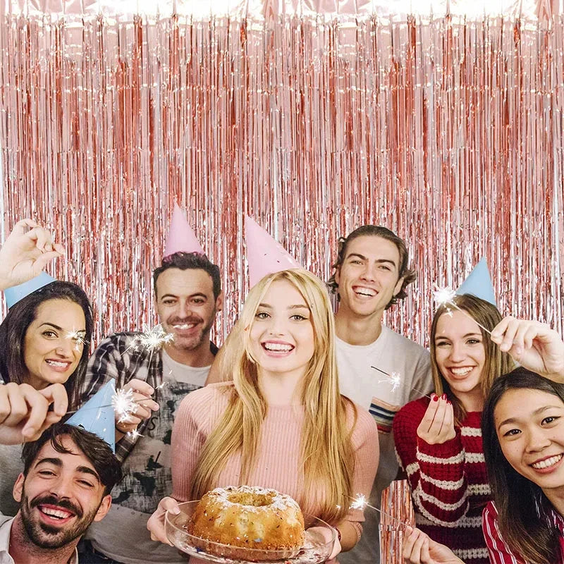 A group of smiling people posing in front of a metallic foil fringe party curtain backdrop.