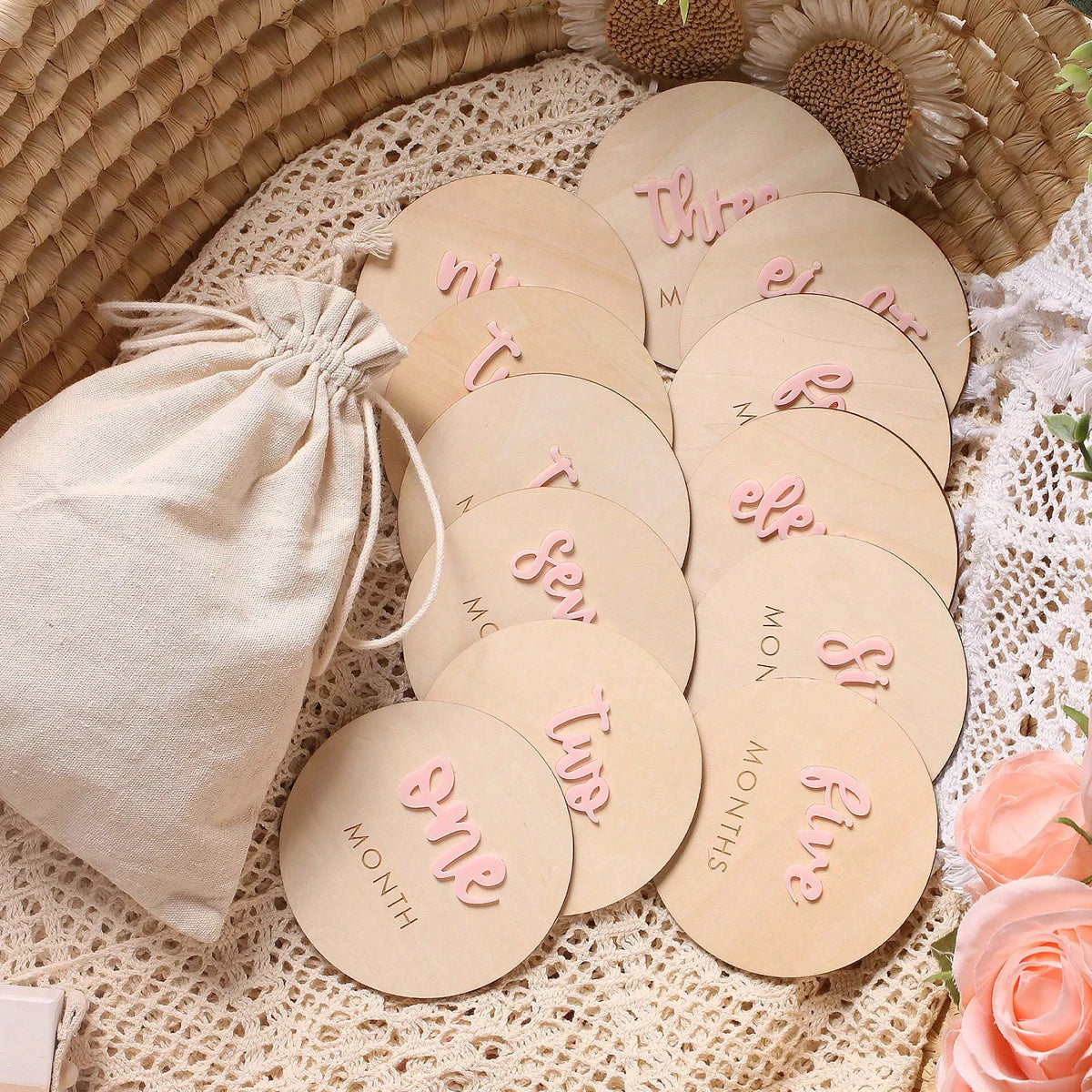 A set of wooden baby milestone cards showing 'one month' through 'five months' in pink and natural wood tones.