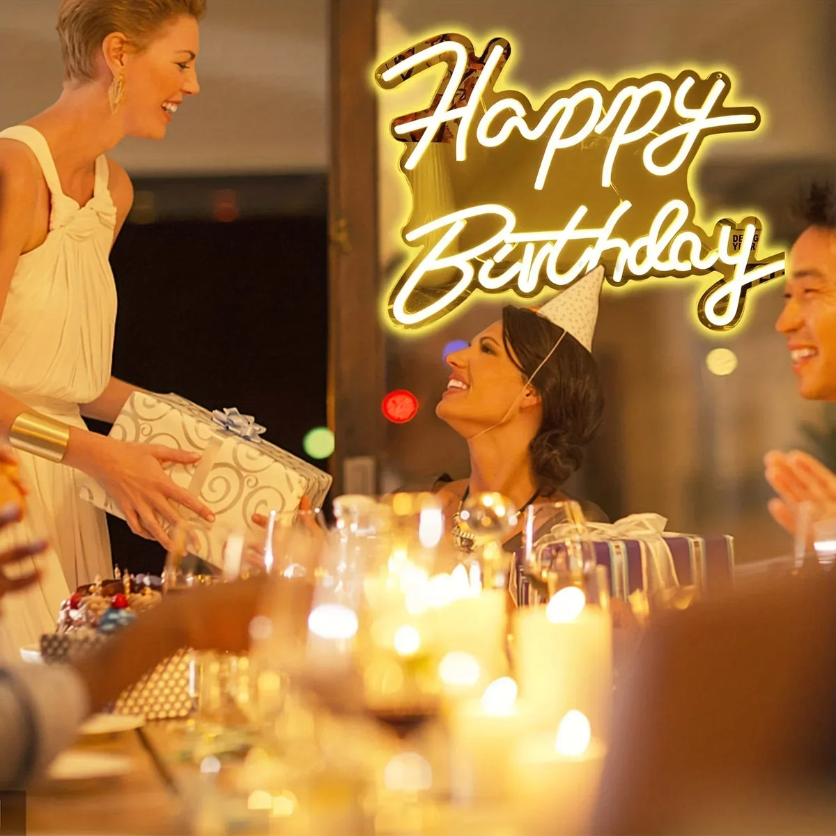A woman smiling while a neon sign reads Happy Birthday in yellow light on a wooden table.